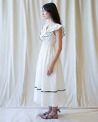 Woman wearing a white dress with black trim against a plain background