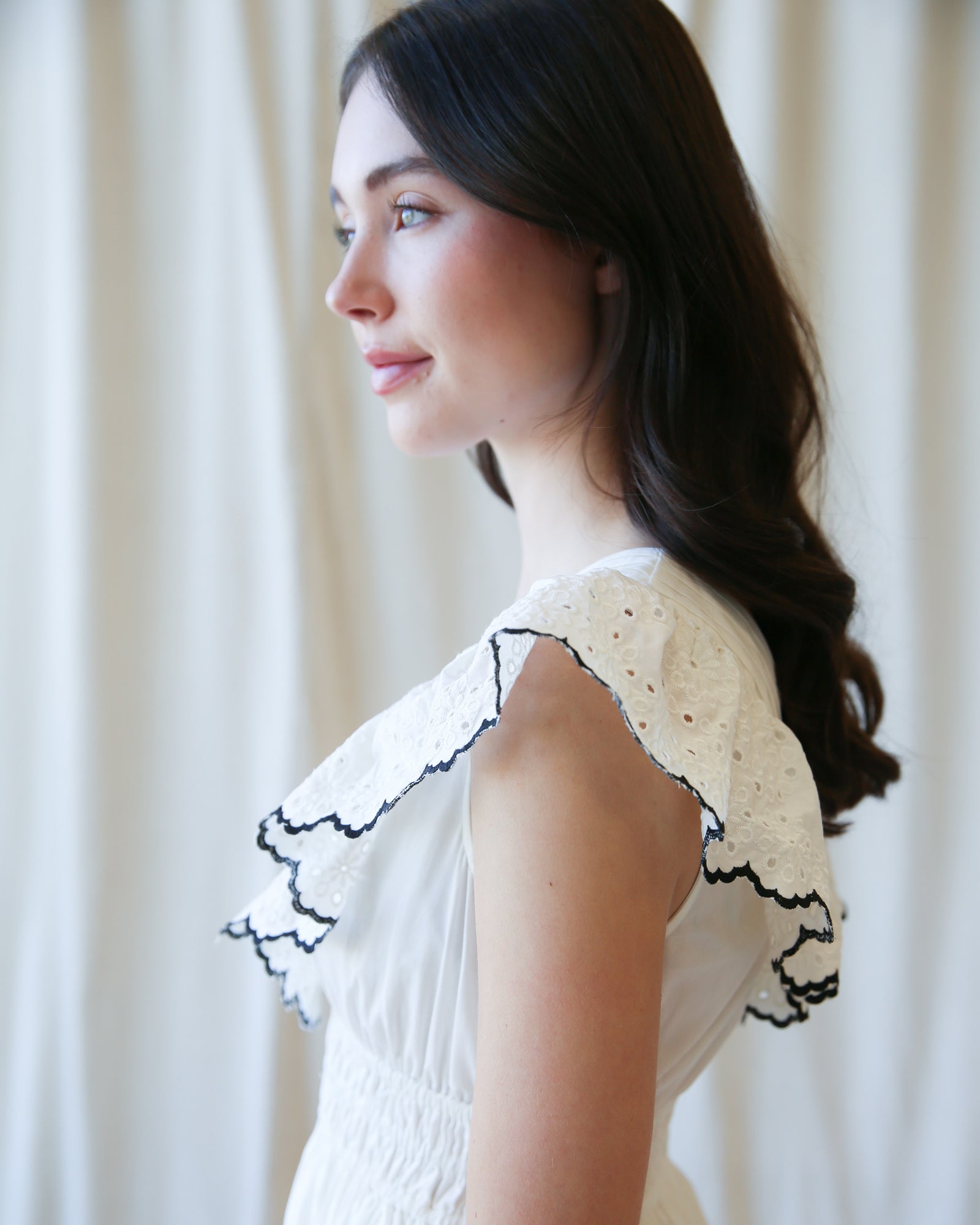 Woman wearing a white top with black lace details against a neutral background