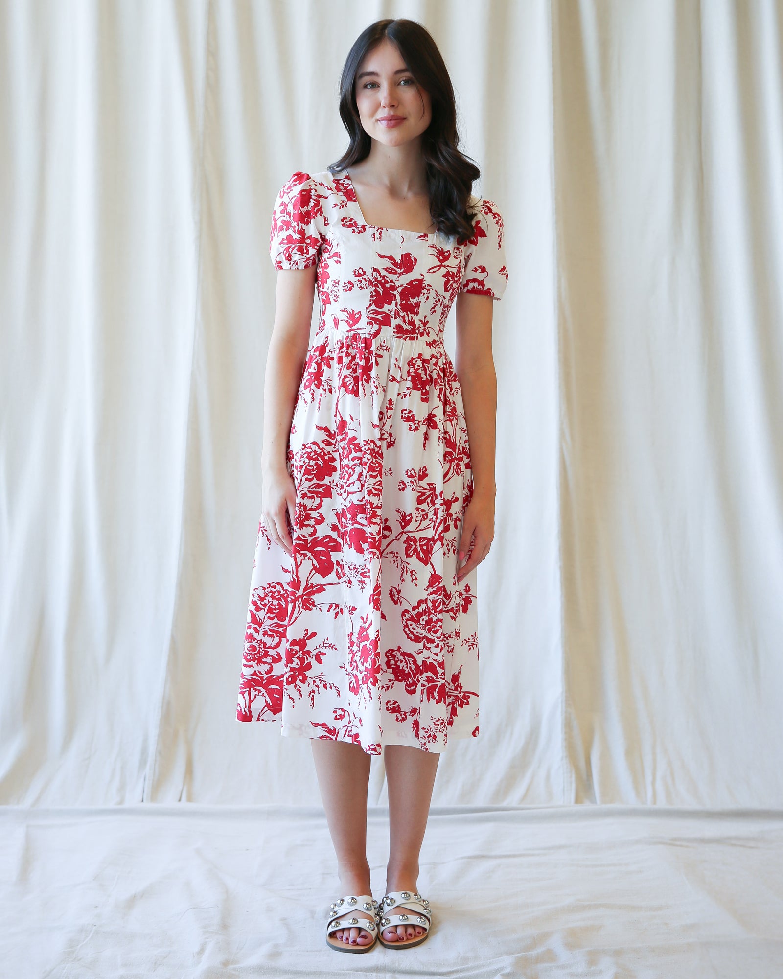 Woman wearing a white dress with red floral pattern against a plain background