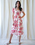 Woman wearing a white dress with red floral pattern against a plain background