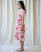 Woman wearing a red floral dress against a white curtain background