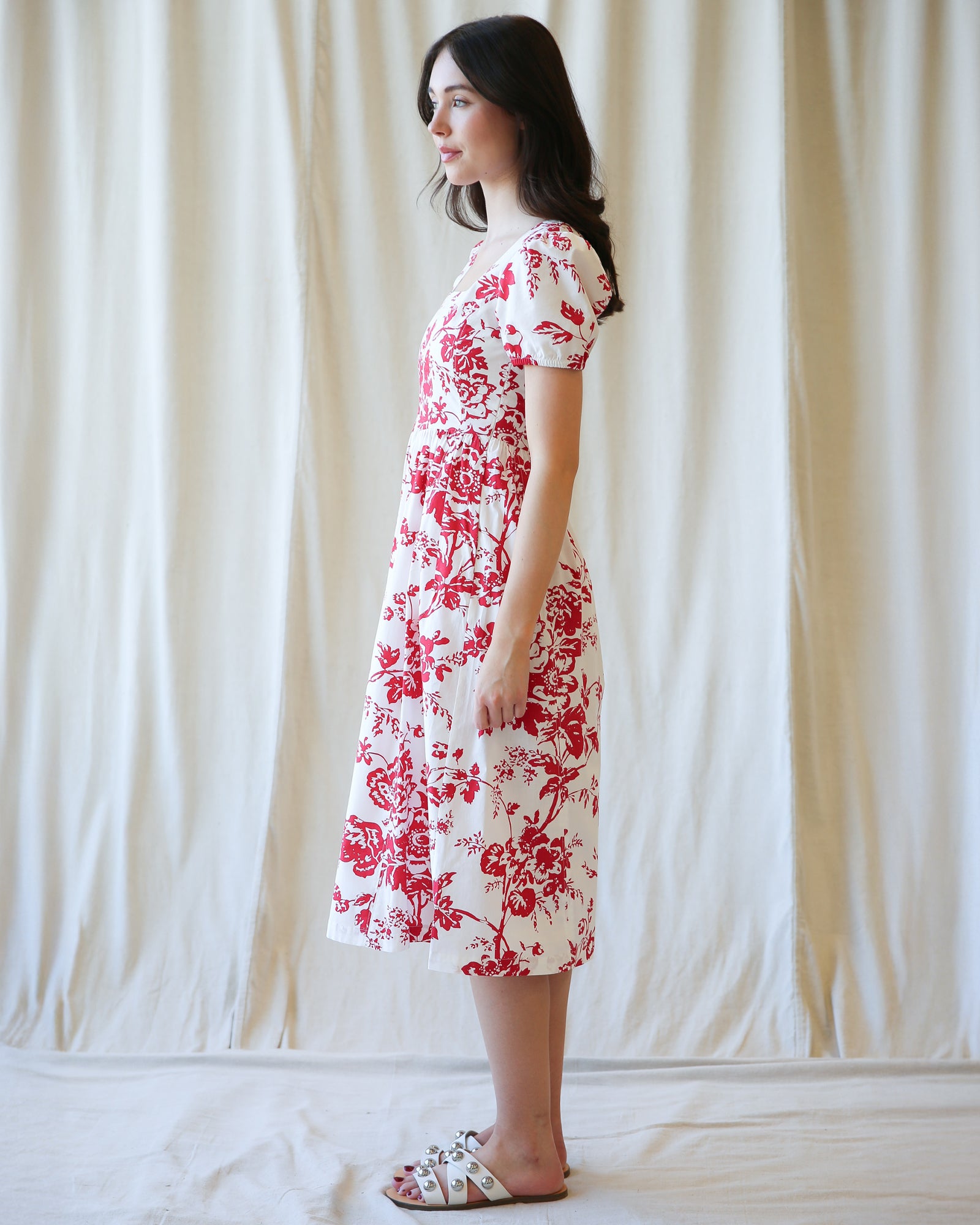 Woman wearing a red floral dress against a white curtain background