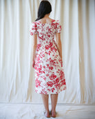 Woman wearing a red floral dress against a white curtain background