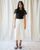 Woman wearing a black top and white button-up skirt against a plain background