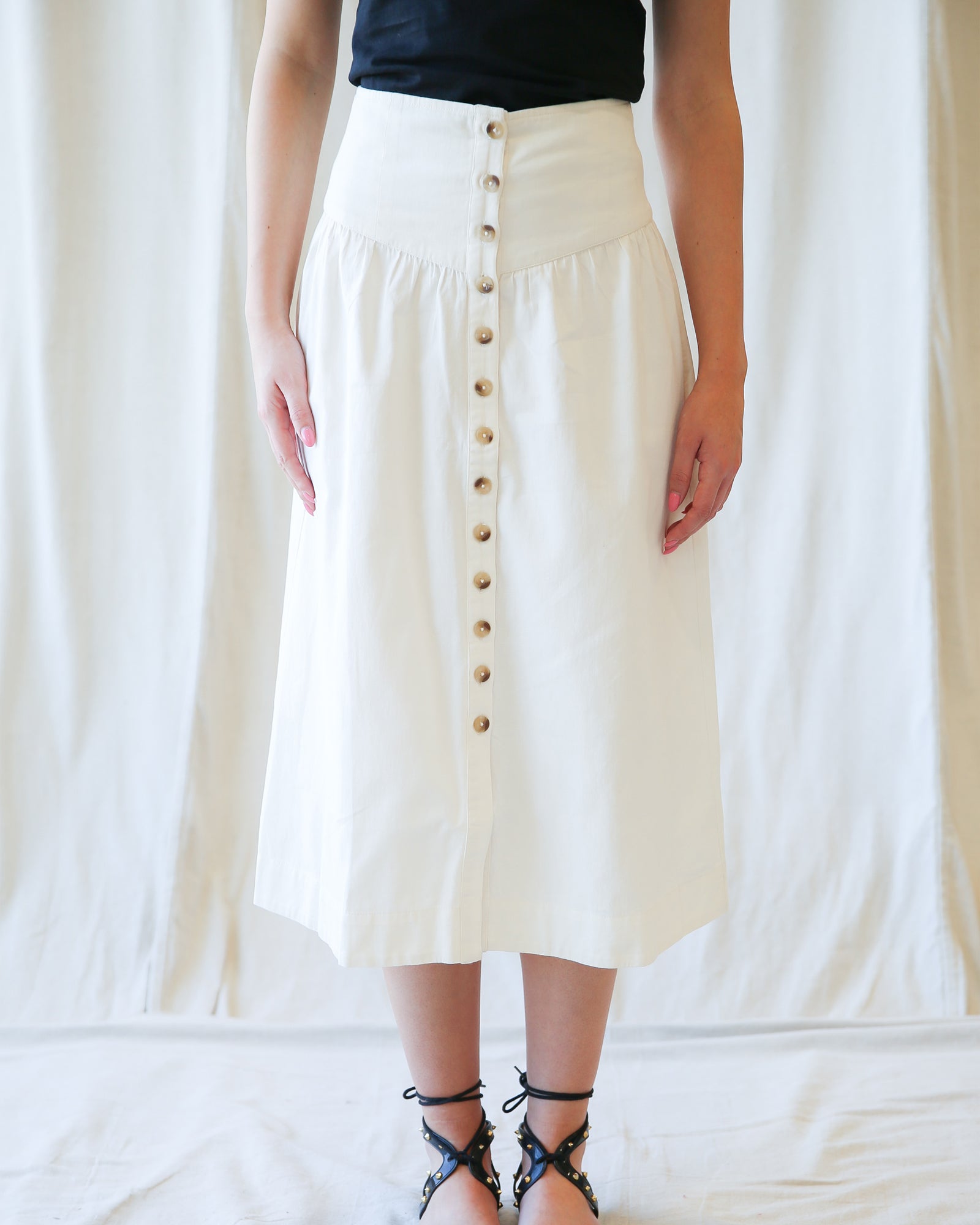 Person wearing a white skirt with buttons against a plain background