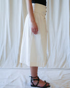 Person wearing a white skirt with button details on a plain background