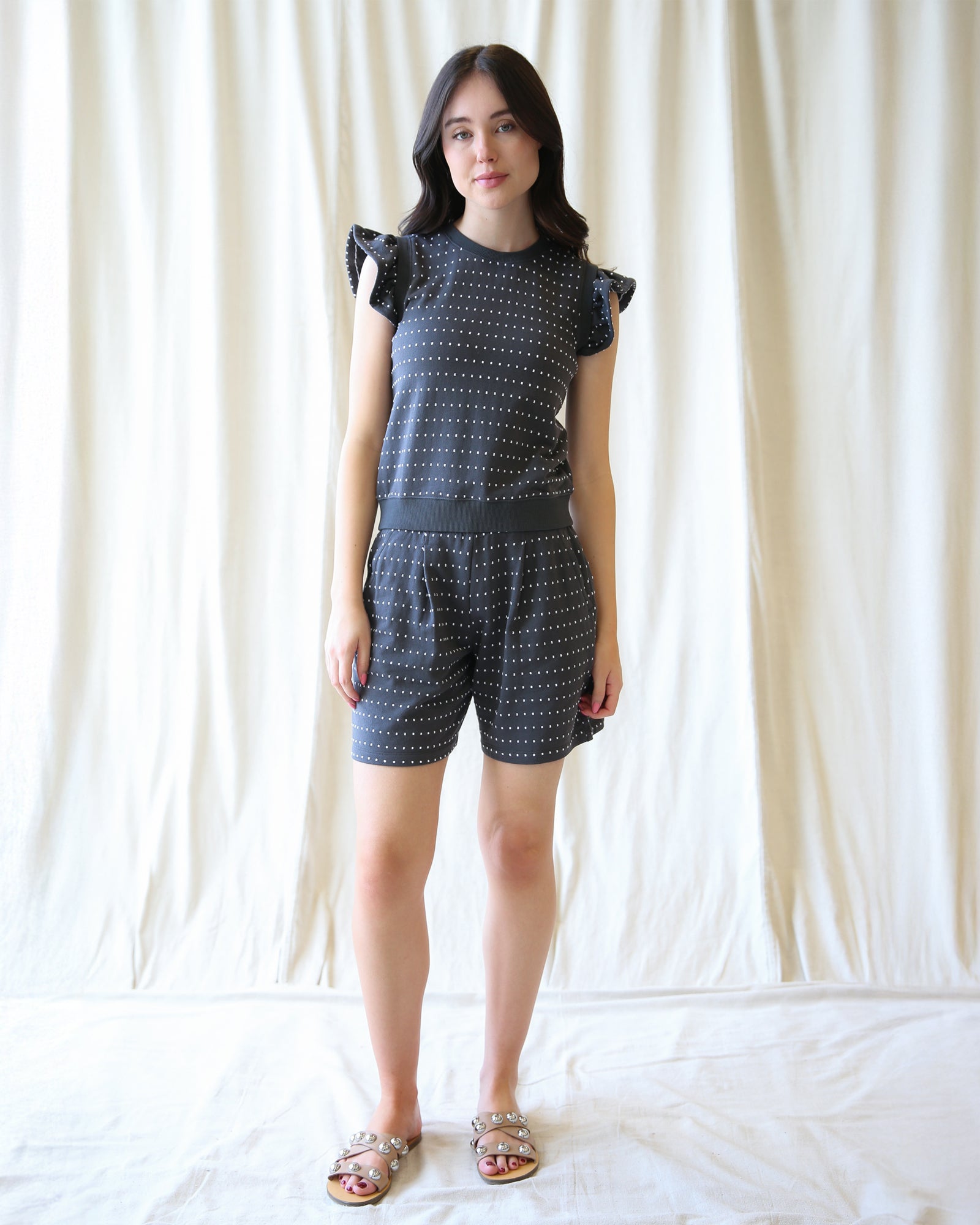Woman wearing a matching top and shorts set against a white curtain background