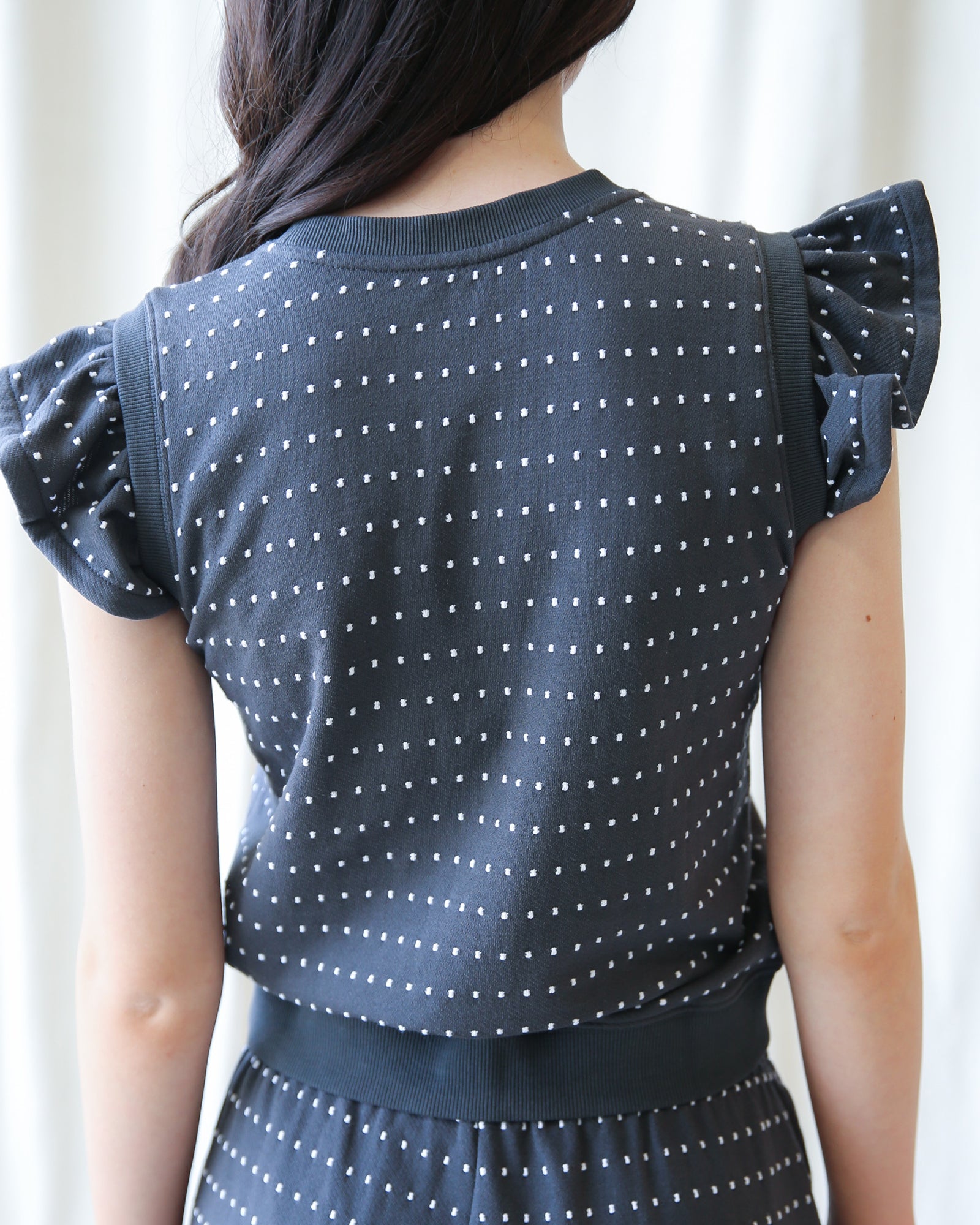 Person wearing a navy blue top with white polka dots and matching skirt against a white background