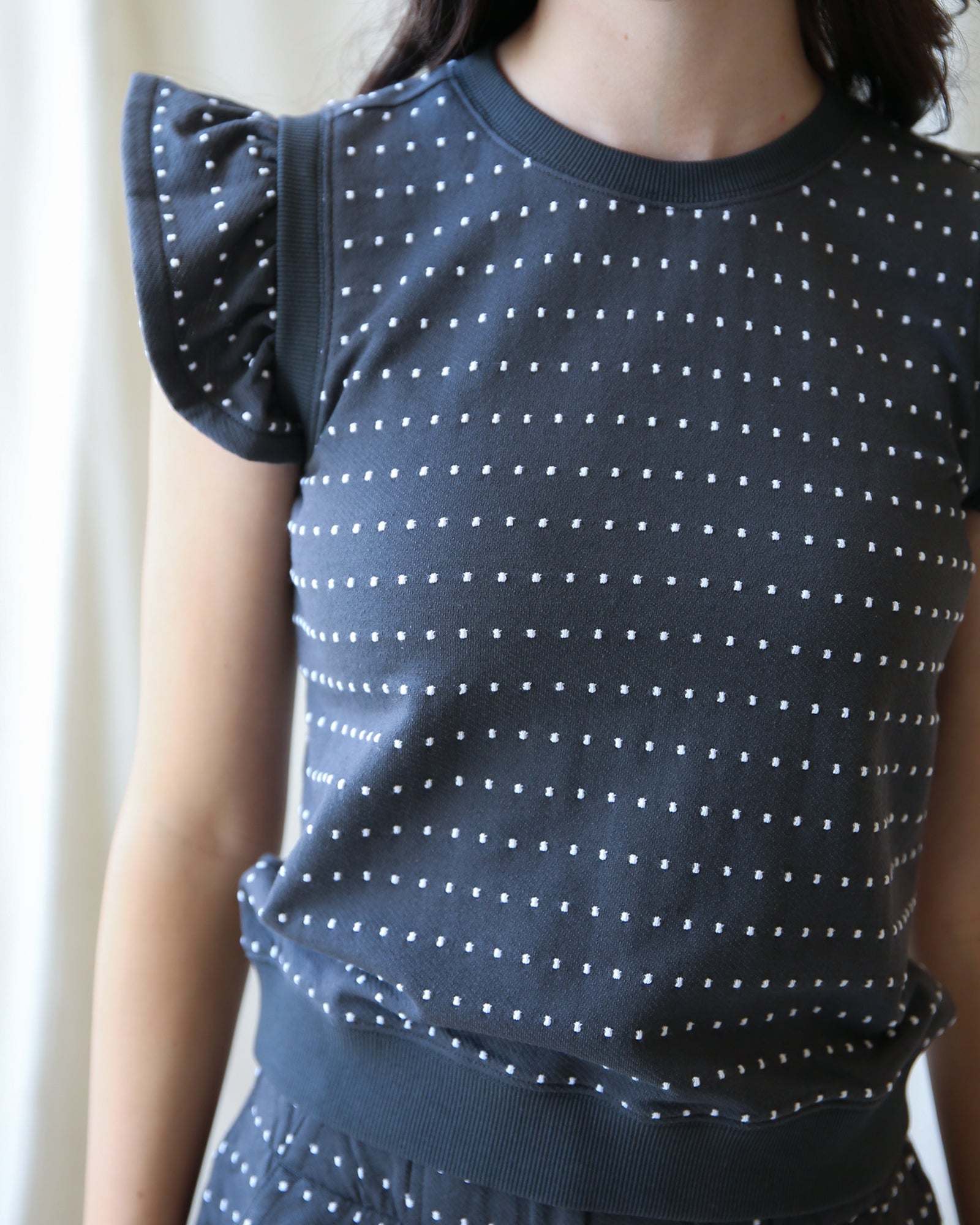 Black top with white polka dots worn by a person, against a neutral background