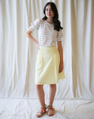 Woman wearing a striped shirt and yellow skirt against a white curtain background
