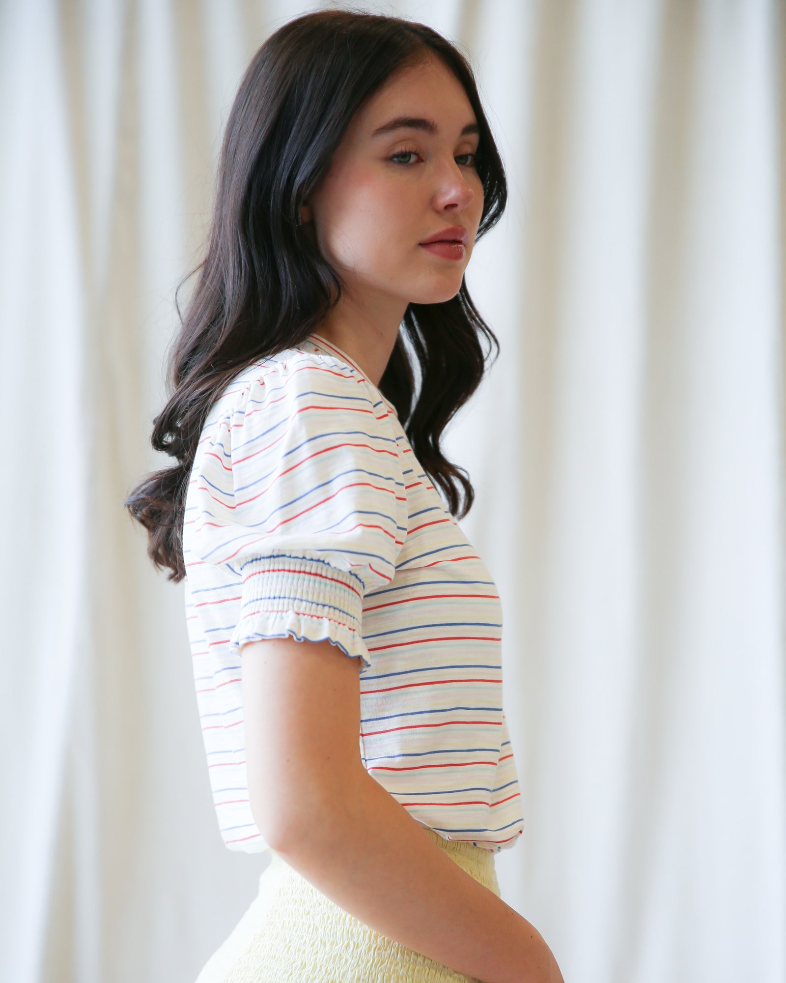 Woman wearing a striped shirt against a white curtain background