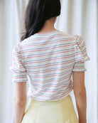 Person wearing a striped shirt with short sleeves against a white curtain background