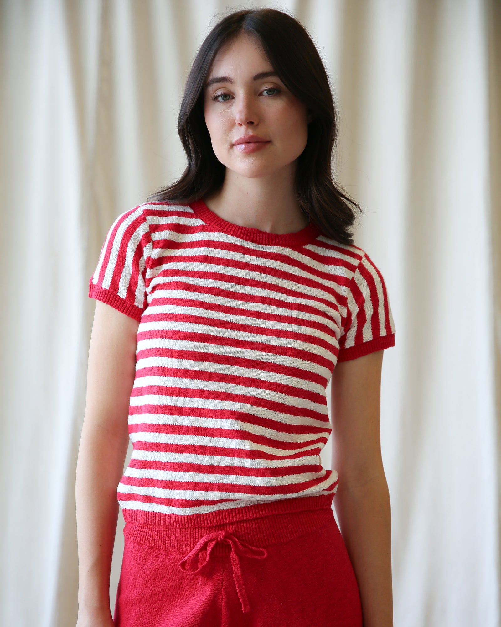 Woman wearing a red and white striped shirt and red pants against a white curtain background