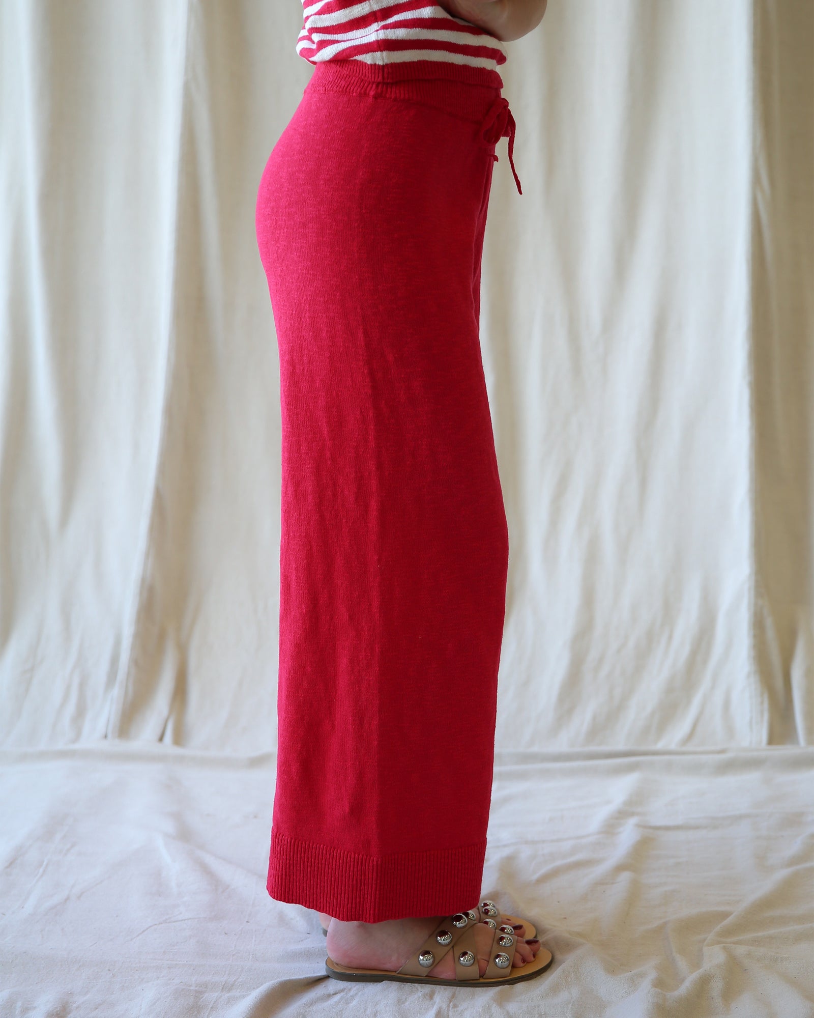 Person wearing red pants and a striped shirt against a white curtain background