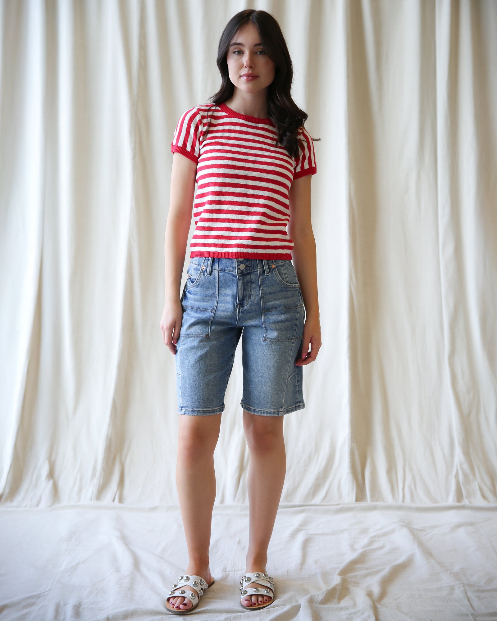 Woman wearing a red and white striped shirt and blue denim shorts against a plain background