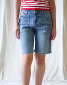 Person wearing blue denim shorts and a red and white striped shirt against a plain background