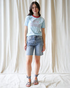 Woman wearing a light blue t-shirt with 'Sun Kissed' text and denim shorts against a white background