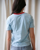 Person wearing a light blue t-shirt with a red collar against a plain background