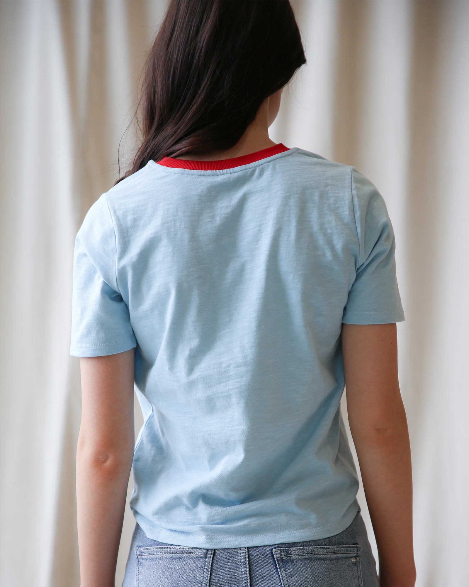Person wearing a light blue t-shirt with a red collar against a plain background