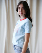 Woman wearing a light blue t-shirt with red text against a white curtain background