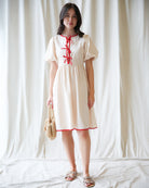 Woman wearing a white dress with red accents against a plain background