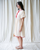 Woman wearing a white dress with red trim against a white curtain background
