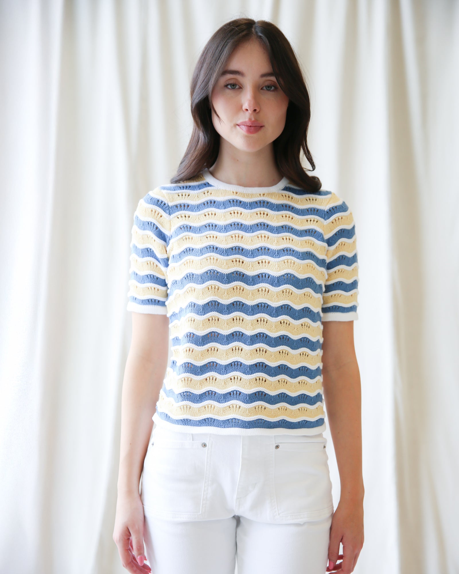 Woman wearing a blue and yellow patterned shirt against a white curtain background