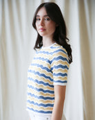 Woman wearing a yellow and blue striped shirt against a white curtain background