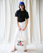 Person wearing a black top, white pants, and a blue cap, holding a tote bag with 'Berry Farm' branding.