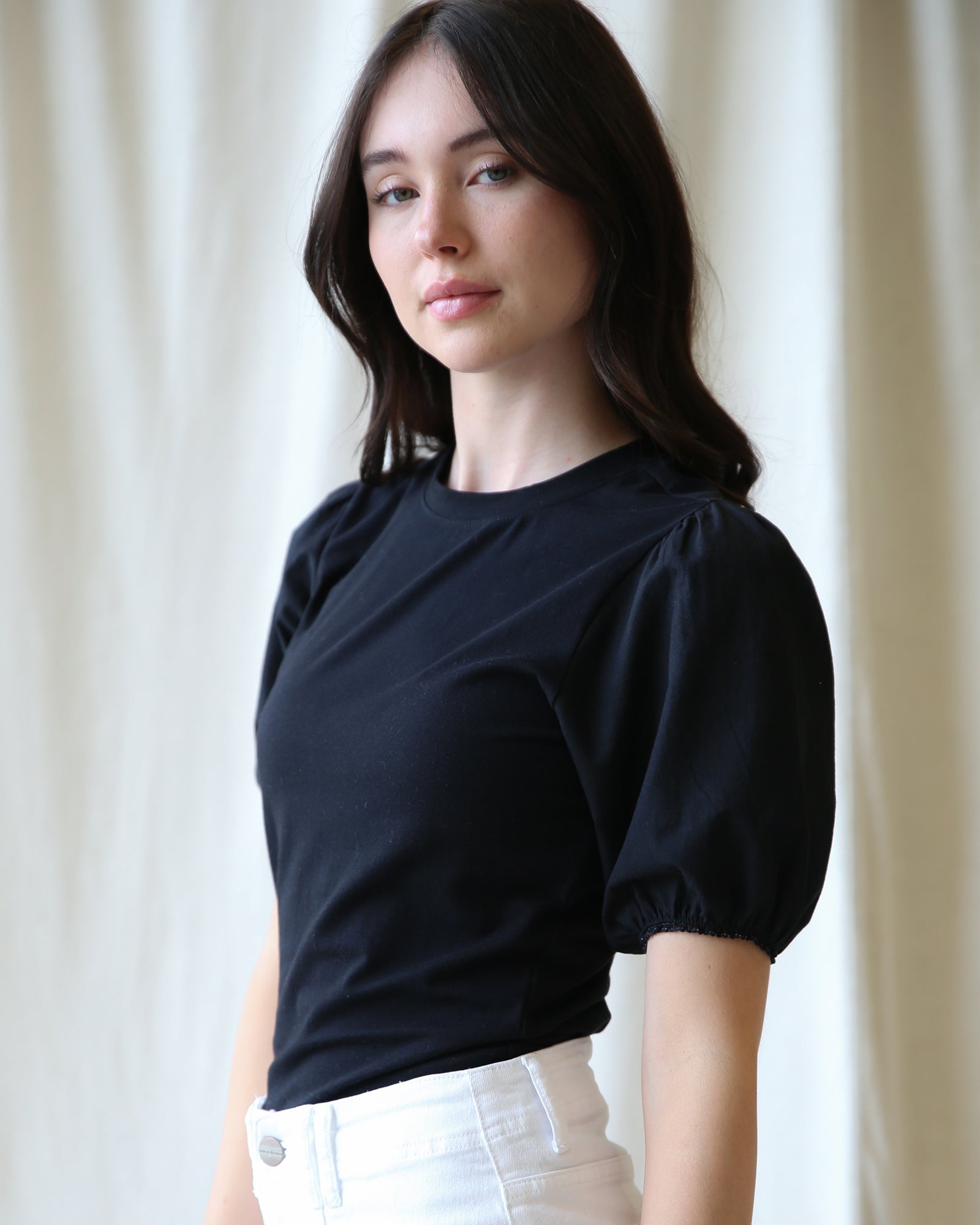 Woman wearing a black top with puff sleeves against a white curtain background
