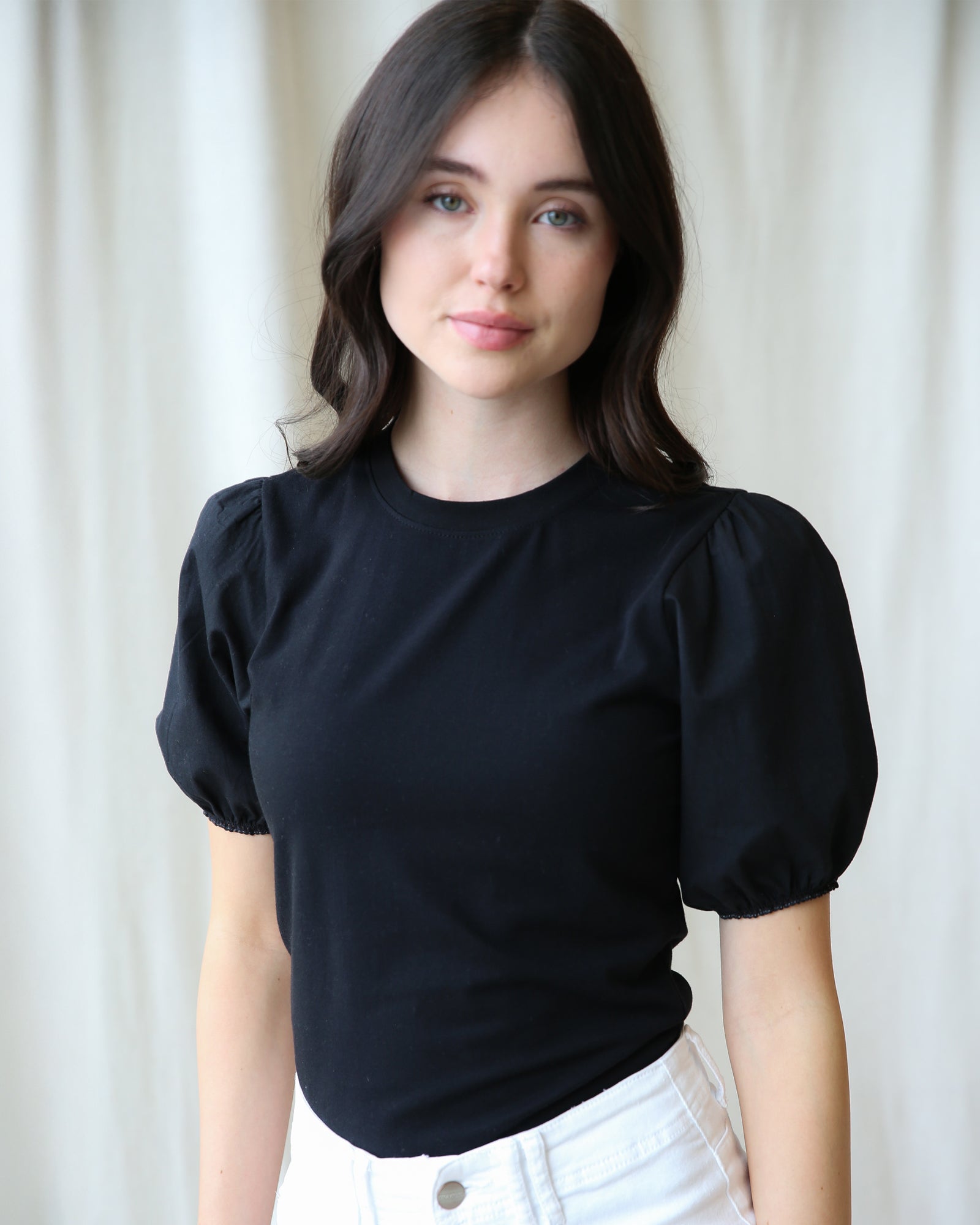 Woman wearing a black top with puffed sleeves against a white background