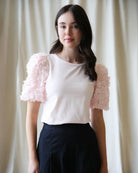 Woman wearing a white top with pink floral sleeves against a plain background