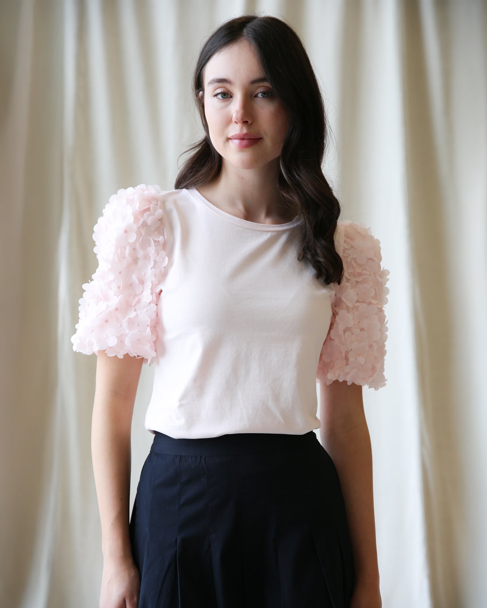 Woman wearing a white top with pink floral sleeves against a plain background