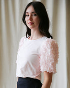 Woman wearing a light pink blouse with floral sleeves against a neutral background