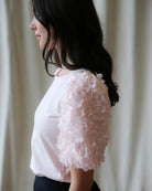 Woman wearing a light pink blouse with floral details against a neutral background