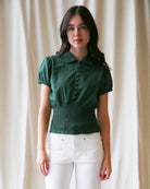 Woman wearing a green blouse with puff sleeves against a beige curtain background