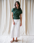 Woman wearing a green top and white pants against a plain background