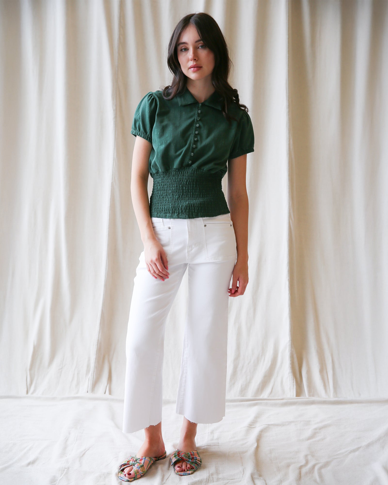 Woman wearing a green top and white pants against a plain background