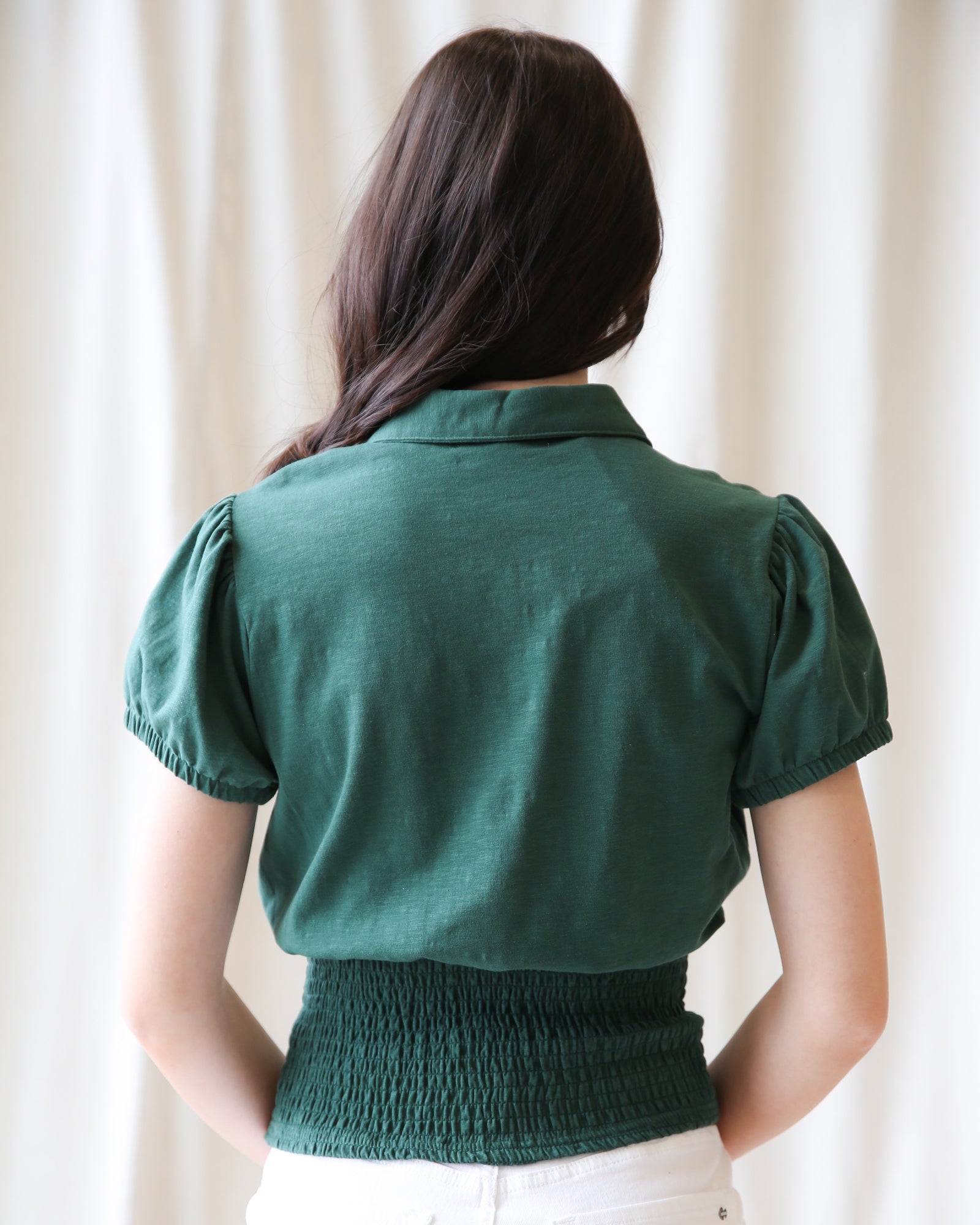 Person wearing a green blouse with puff sleeves against a white curtain background