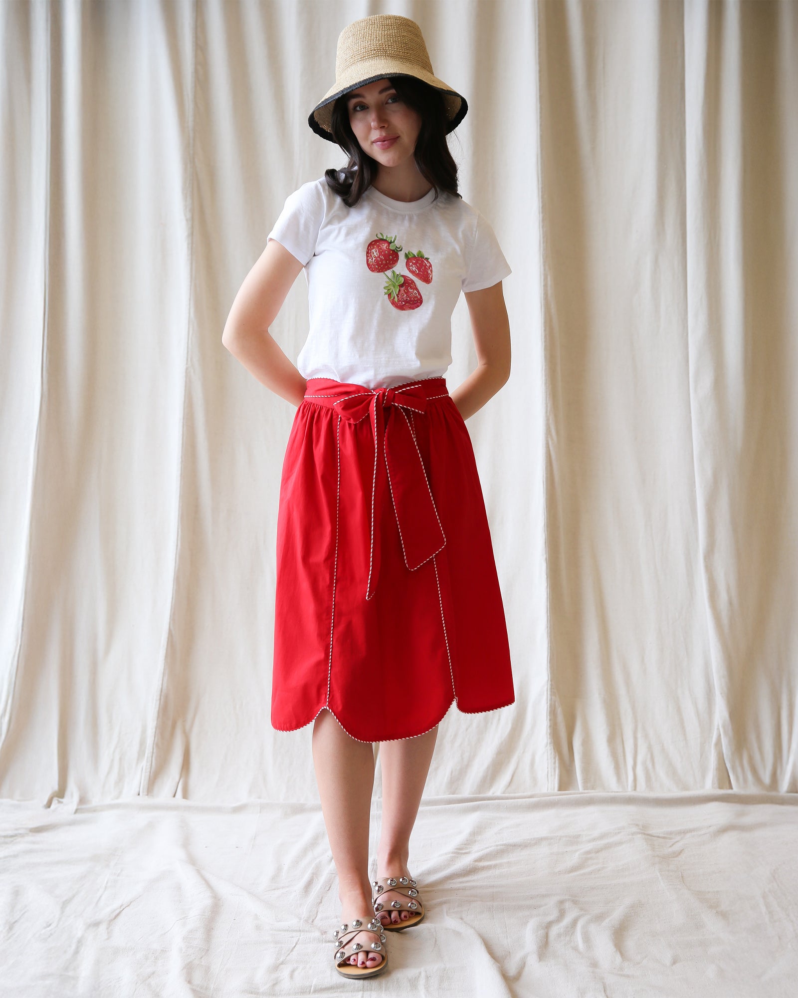 Person wearing a white t-shirt with strawberry design and red skirt against a plain background