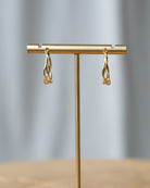 Gold earrings on a gold T-shaped stand against a gray background