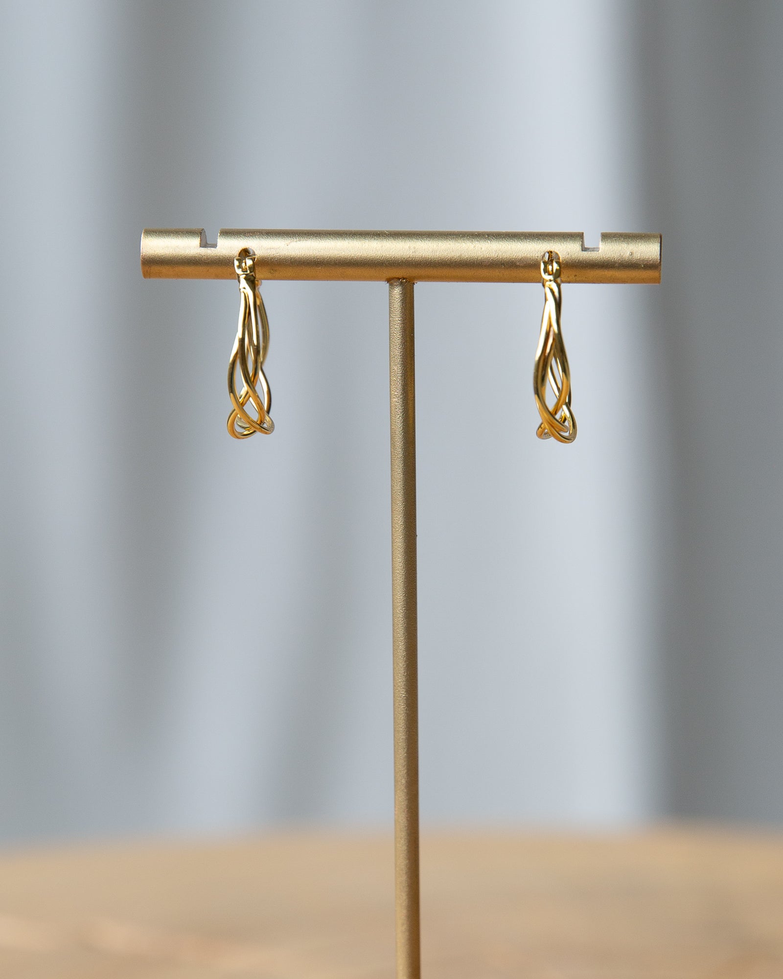 Gold earrings on a gold T-shaped stand against a gray background