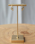 Gold earring stand with gold earrings on a wooden surface