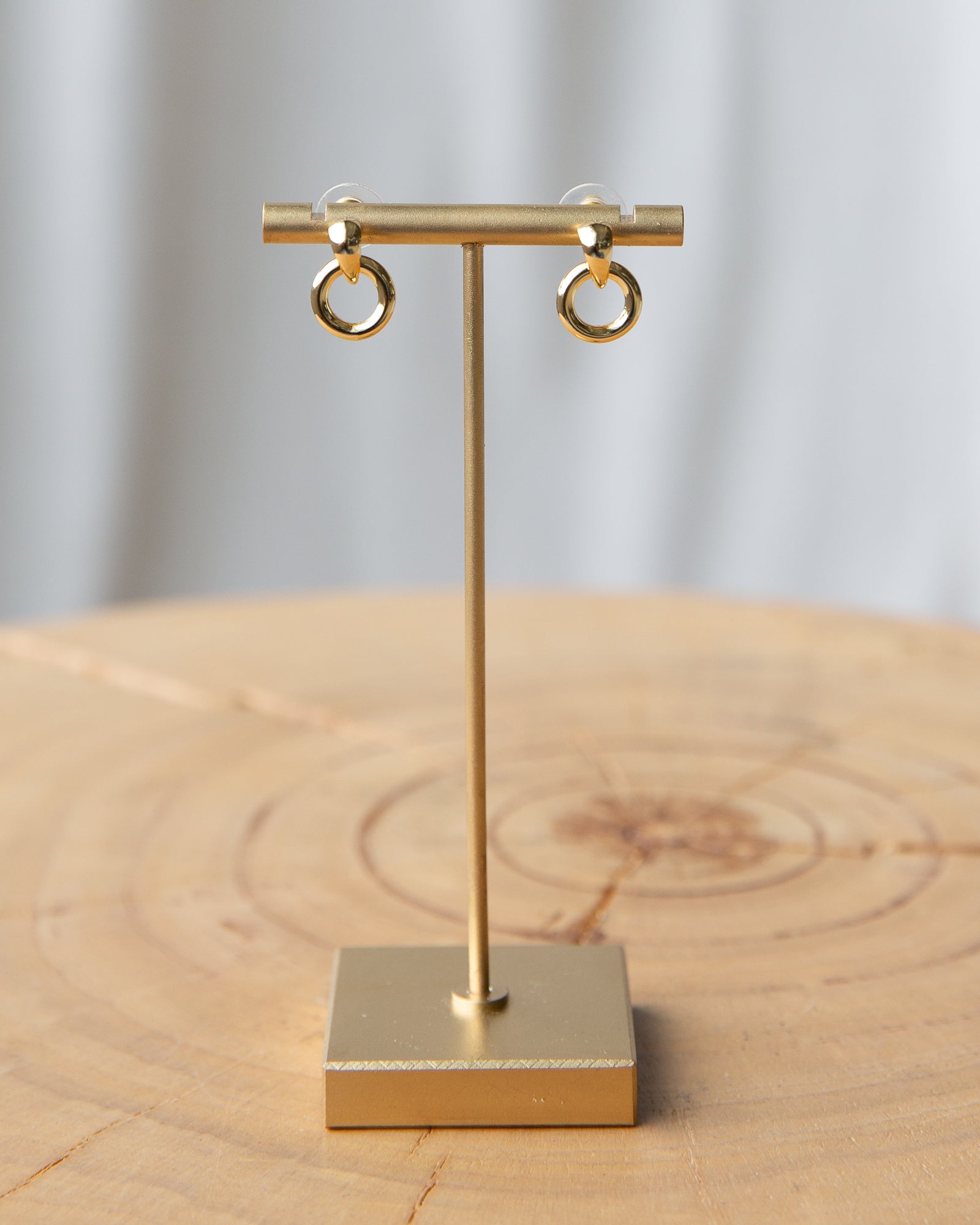 Gold earring stand with gold hoop earrings on a wooden surface