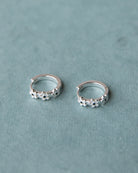 Pair of silver hoop earrings with floral designs on a light blue background