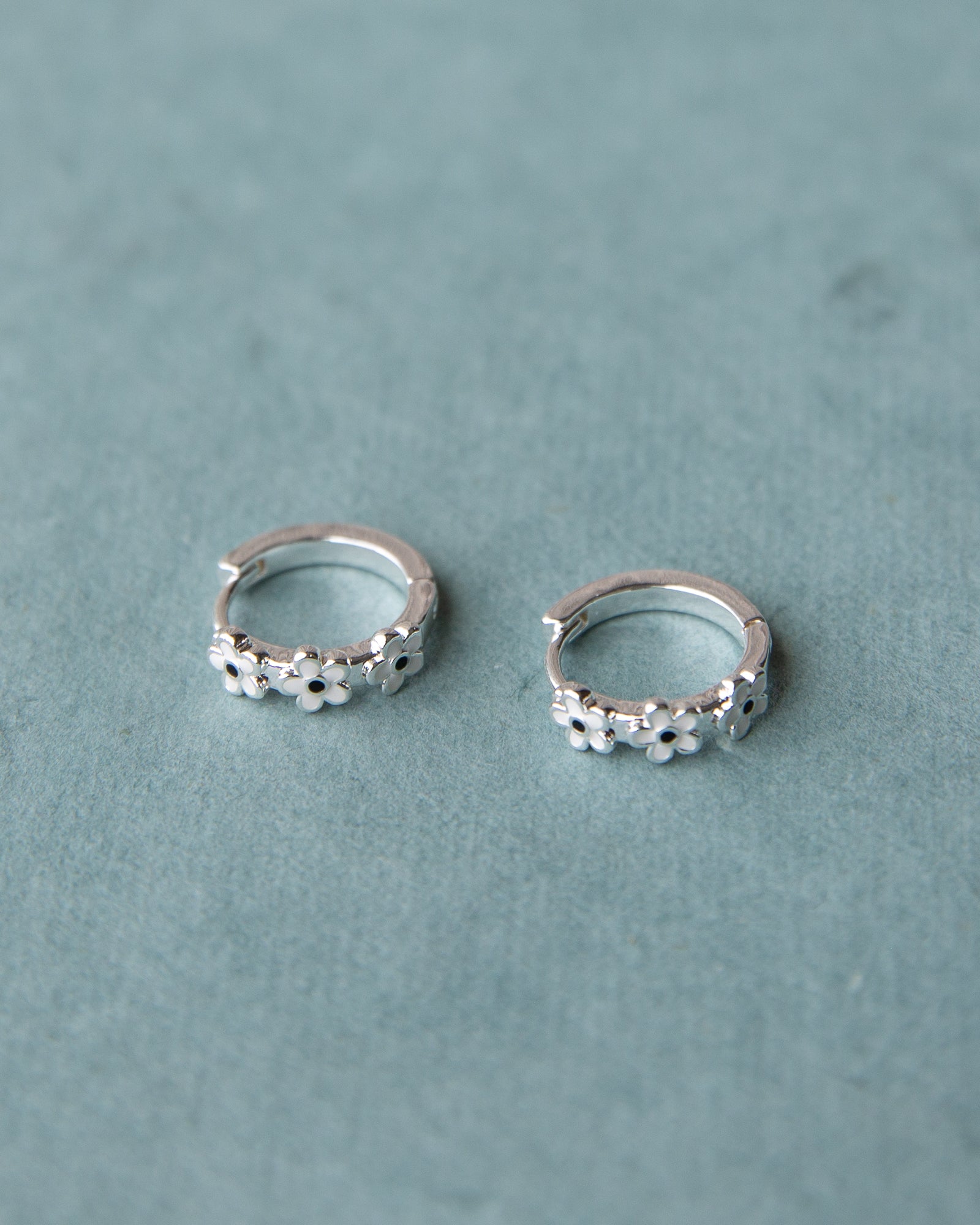 Pair of silver hoop earrings with floral designs on a light blue background