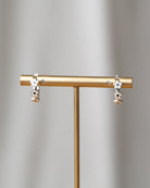 Pair of earrings on a gold stand against a gray background