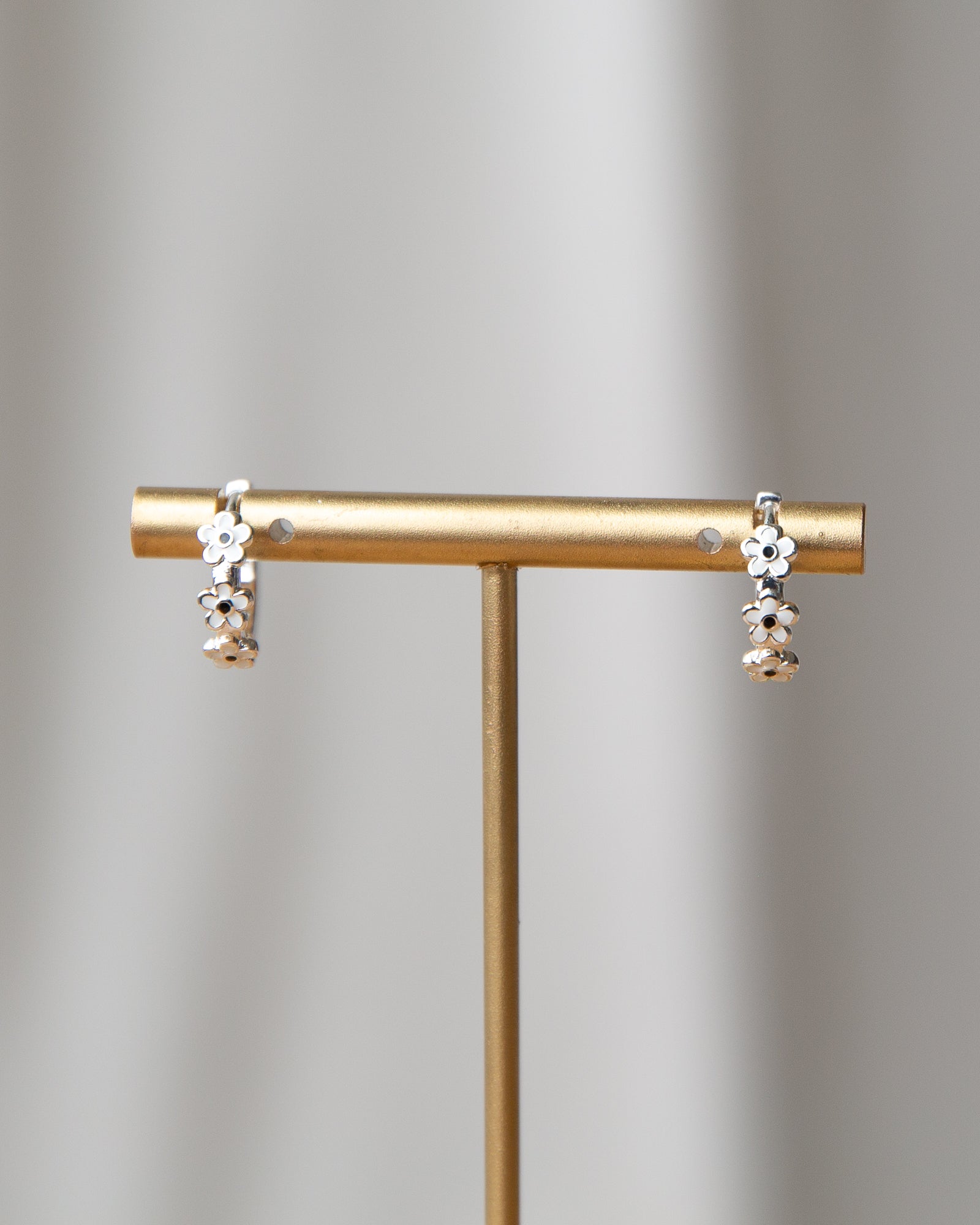 Pair of earrings on a gold stand against a gray background