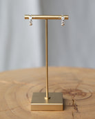 Gold earring stand with earrings on a wooden surface and gray background