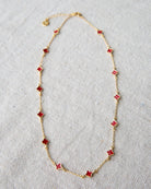 Gold necklace with red flower-shaped pendants on a light gray background
